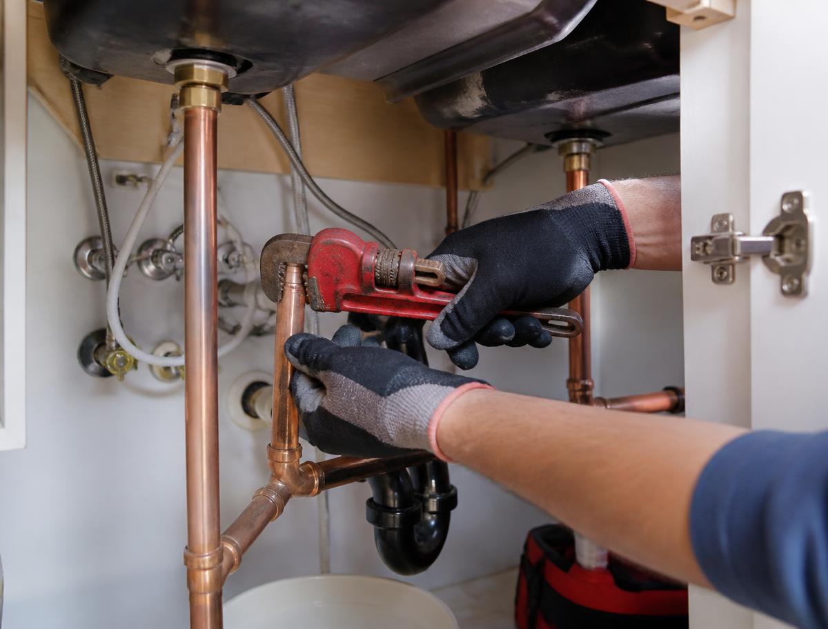 Plumber tightening a copper supply line under a kitchen sink